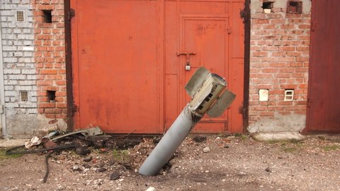 Close-up view 4k stock video footage of real unexploded military missile, torpedo or shell stuck in ground near doors of garages outdoors. Moments of dreadful war of Russia against Ukraine in 2022