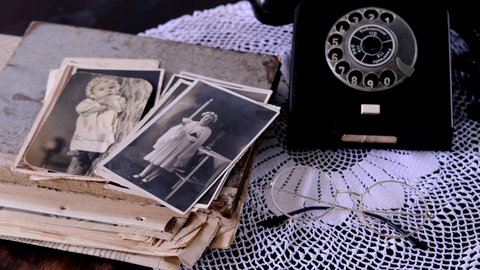 middle-aged woman's hands hold old photos 50s, 60s, retro phone, photo albums, handmade lacy on table, concept of genealogy, memory of ancestors, family tree, childhood memories