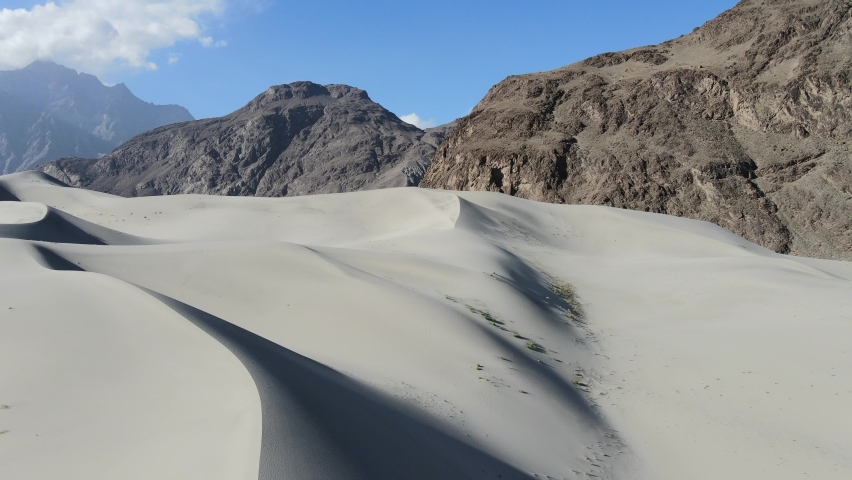 aerial drone flying backwards revealing large sand dunes in the Cold Desert of Skardu Pakistan overlooking large mountains