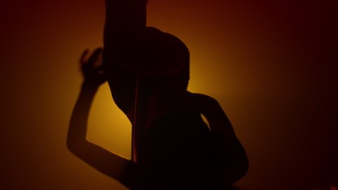 Silhouette of woman performing poledance in spotlight strip club. Unknown fit girl dancing seductive on nightclub pole. lady dancer making erotical show spinning on pylon upside down.