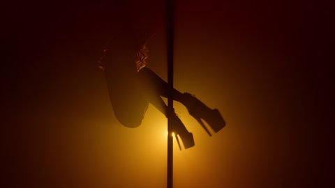 Flexible woman silhouette practicing poledance in nightclub spotlight. lady turning round pole making acrobatic tricks on strip show. Sensual girl pole dancing sexually in soft backlight