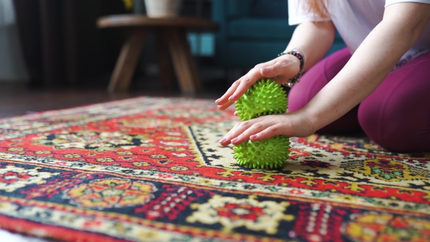 Hands of a woman doing exercises with green pilates balls in her living room on the floor