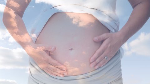 Mid section of caucasian pregnant woman rubbing her tummy against clouds in blue sky. medical and pregnancy concept
