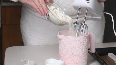 A woman adds flour to a container, makes dough. The ingredients for making the cake are laid out on the table. Cooking biscuit cake Dairy girl.