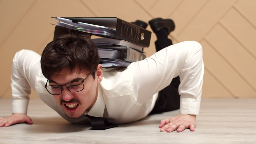 Male office worker is pinned down by stack folders of working documents and tries to get up from floor, front view. Male manager is trying to get up pinned down by stack of folders Royalty-Free Stock Footage #1089478435