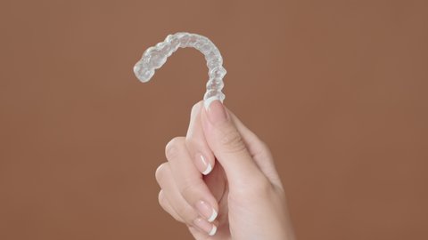 Close up young woman hand is holding Invisalign over brown background 