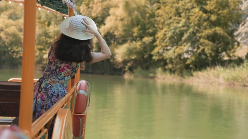 Beautiful young woman in a straw hat and dress stands and sightseening. Back view. Concept of excursions by river bus and summer vacations.