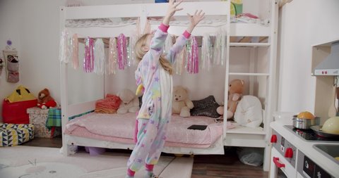 Adorable little 7 year old girl playing in the children's room in a unicorn costume with many toys. Kid joy with unicorn pajamas.