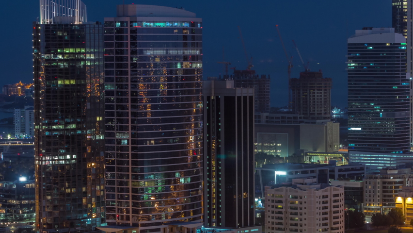 Office buildings in Dubai Internet City and Media City district aerial night to day transition timelapse. Traffic on junction and skyscrapers with sunrise and sun reflected from glass