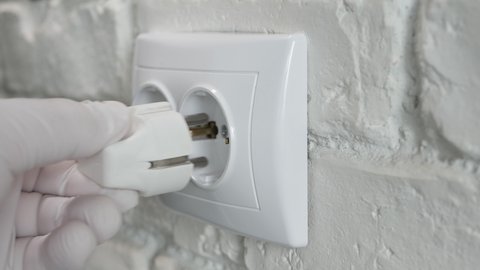 Man Plugs a Power Cord in an Electrical Outlet on a Wall. Connecting a Device to Electricity Power.