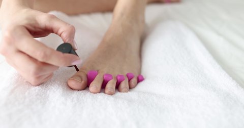 Woman paints her toenails while sitting on bed closeup