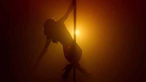 Silhouette attractive woman pole dancing emotionally wearing shorts on night club stage. Sporty girl dancer moving body eroticly on pylon. lady spinning seductive on nightclub strip show.