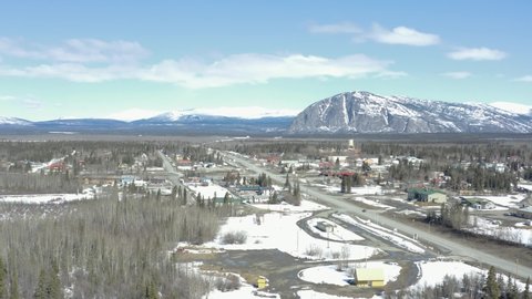 Drone flight towards the Village of Haines Junction in the Yukon with the Dezadeash river in the foreground and paint mountain in the background on a sunny day in Spring.