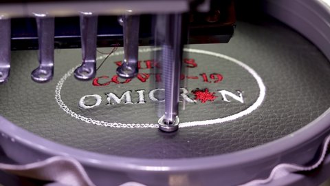 Machine embroidery of the inscription virus covid-19 Omicron on black leather with red and white thread. Machine embroidery design, close up 4k video. Selective focus.
