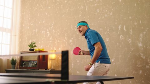 Charismatic and attractive old man playing the ping pong at home he feeling excited smiling large catch the balls with the red racket