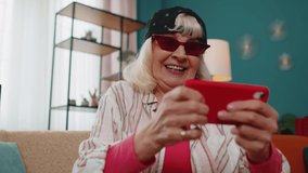 Worried funny stylish elderly granny woman enthusiastically playing shooter online video games on mobile phone at home on sofa. Senior old grandmother using smartphone gadget app with drive simulator - Powered by Shutterstock - Get 15% off with code: PIKWIZARD15