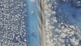 Aerial video of winter road surrounded by birch forest. Drone flight over of trees covered with hoarfrost and snow. Natural winter background. Camera pointed down.
