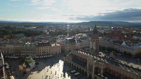 Aerial drone view of Krakow main market square, clock tower, St. Mary's church and people walking around in sunny day. Krakow, Poland.