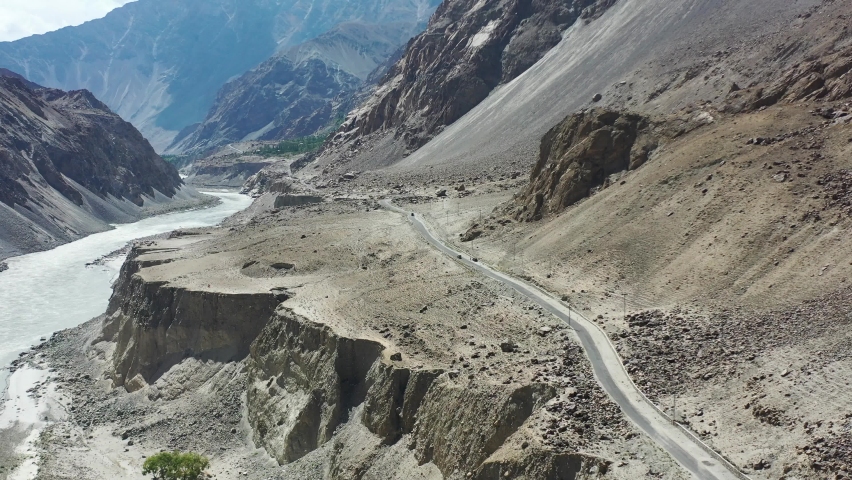 aerial drone overlooking a dirt highway road and large mountain cliff with the Indus River Valley below in between the canyon of the rugged Skardu mountains on a sunny summer day