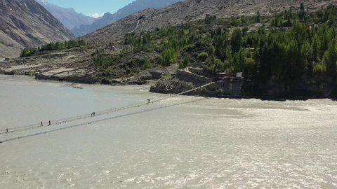 aerial drone of the famous Hussaini Bridge as tourists cautiously cross the bridge over a fast paced river below in the mountains of Hunza Pakistan.