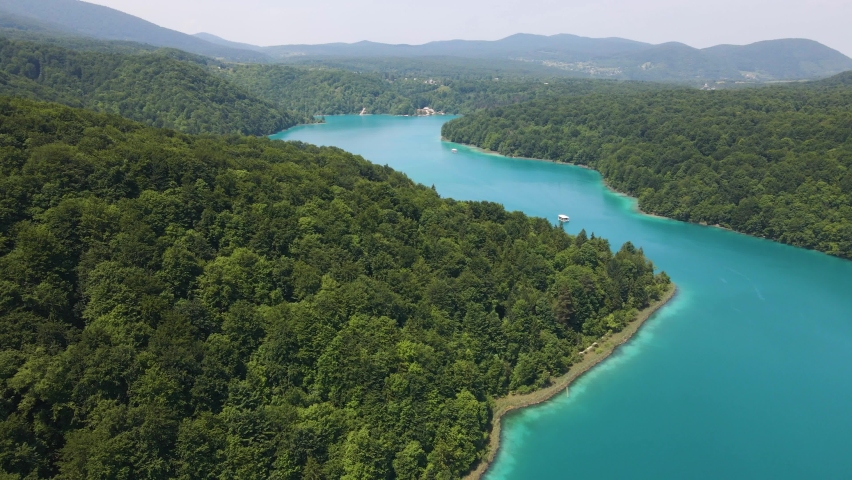 View from above of the Plitvice Lakes National Park with many green plants and beautiful lakes, drone flight over the strait and a boat passing through it. Croatian nature