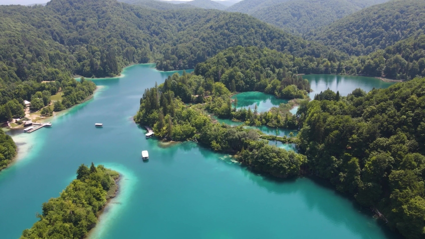 View of the Plitvice Lakes National Park with many green plants and beautiful lakes and waterfalls drone flight over the bay and boats. Cascading blue lakes surrounded by forest in Croatia