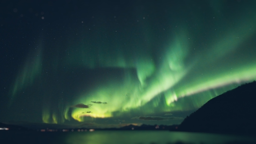 Aurora borealis above the fjord. Street lights and car lights flash in the background. Timelapse. Royalty-Free Stock Footage #1089499071