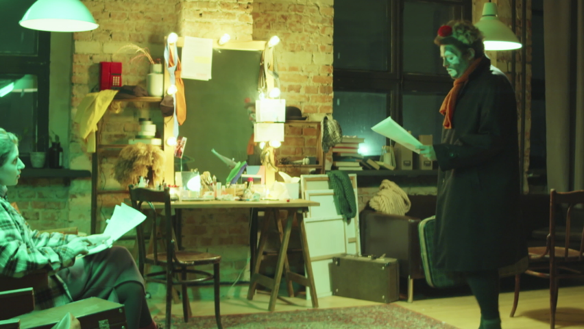 Male clown walking with suitcase in dressing room, sitting on chair and discussing circus act on paper with female scriptwriter during rehearsal