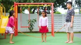 Group of little kids looks happy while playing jump rope together at the playground. Shot in 4k resolution