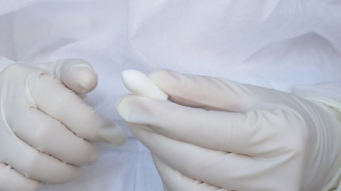 Suppositories in woman hands, white gloves. nurse or doctor, medical assistant, in white disposable robe holds a suppository,no plastic pack. Suppository for anal or vaginal use. temperature, fever