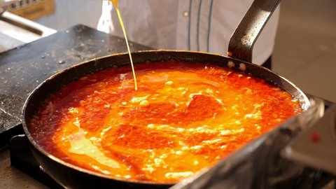 A close-up of the chef pouring eggs into a frying pan with butter and tomatoes, cooking a Turkish omelet with tomatoes in the kitchen of the hotel restaurant.