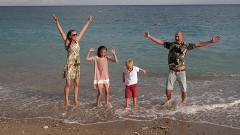 A large family with children is relaxing and having fun on the beach, they jump and laugh near the water.