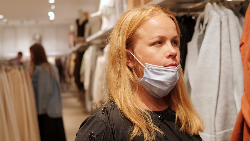 Portrait of a young woman with long blonde hair wearing a medical mask in a clothing store in the mall.