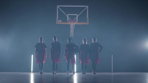 Slow motion performance, team of basketball female players walks through the gym in contour lighting, the international women's basketball championship, team stance in front of the camera.