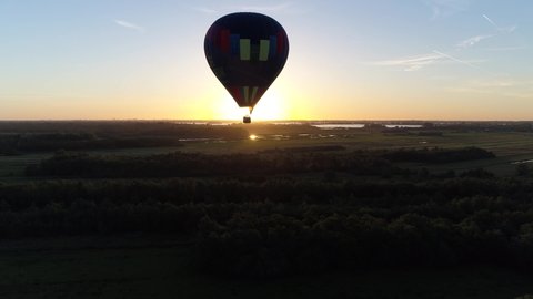 Aerial bird view near hot air ballon in flight during sundown aircraft moving over nature reserve meadows and pastures in far background warm colors of sunset sunlight showing on horizon 4k quality