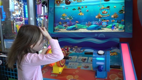 Fishing game. Little girl in the entertainment center. The child plays on token ticket slot machines while the parents go shopping. Perm, Russia, March 31-2022