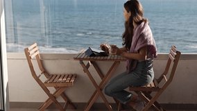A woman is working on a digital tablet with a stylus on the terrace and looking at the sea - Powered by Shutterstock - Get 15% off with code: PIKWIZARD15