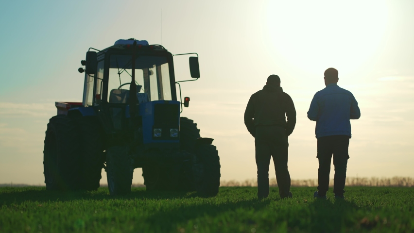 Teamwork concept. Silhouette two male farmers walking in a green field against sunset. Team farmers stand in a field on the background of agricultural machinery. Agronomists discuss harvest. Royalty-Free Stock Footage #1089509941