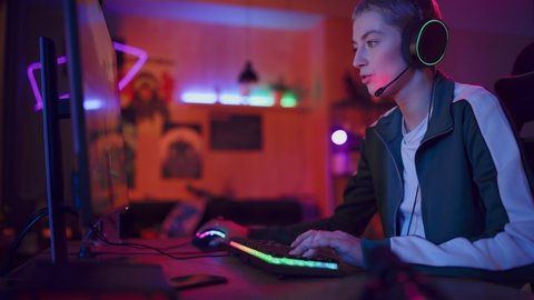 Excited Female Gamer Playing PvP 3D Shooter Video Game in Which Players Fight in a Tournament on Her Personal Computer. Room and PC with Neon Led Lights. Stylish Young Woman in Cozy Room at Home.