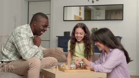 Happy family of three people of different races play chess at home in the living room. Game On, Family Meeting, Multi Ethnic Family, Different Generations.