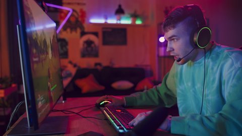 Joyful Gamer Playing PvP Shooter Video Game in Which Players Fight in a Battle Royale Deathmatch on His Personal Computer. Room and PC with Colorful Neon Led Lights. Stylish Man in Cozy Room at Home.