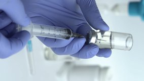 Close-up of Doctor's Hands in Blue Medical Gloves Filling Syringe with Liquid Medication from Glass Vial. Vertical video, 4k