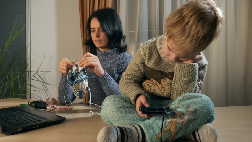 Child Kid Boy Use Watching Smartphone Internet Social Media. Mother Knit with Knitting Needles near Window. Cold Winter Season. 2x Slow motion 60fps 4K Royalty-Free Stock Footage #1089513417