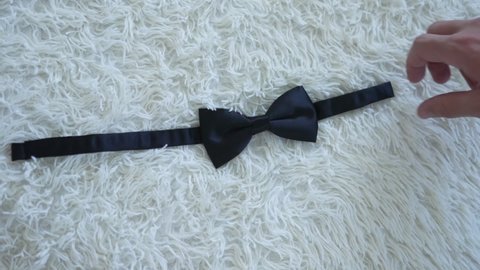 Men's elegant accessory on a blanket with villi. Successful man pulls a bow tie with his hand. Preparing for official party. The butterfly is worn around neck, under collar of shirt. Wardrobe detail