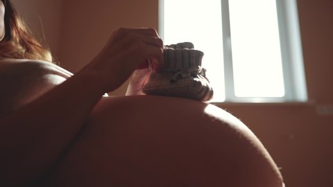 happy pregnant woman. booties baby shoes on the belly of a pregnant woman. pregnancy health procreation concept. close-up belly indoor of a pregnant woman. woman waiting for a newborn baby