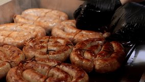 Close-up of cook hands in black gloves turns the sausages on the hot electric grill, close-up 4K video