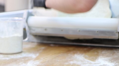 Professional cook kneads the dough and puts it into special rolling machine, close-up 4k footage