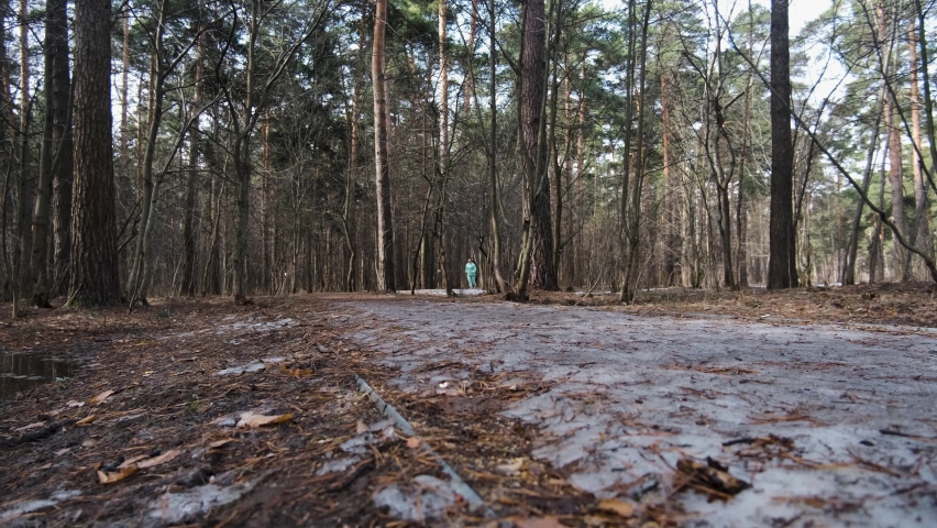 one girl is engaged in berm in the park, she runs from the forest to meet the camera, sunny spring day, a girl with black hair, trees without foliage, the remains of snow are visible on the path