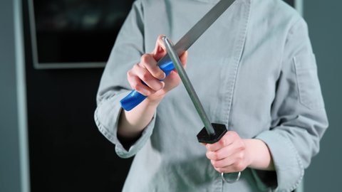 Close up footage of woman chef sharpening knife in kitchen
