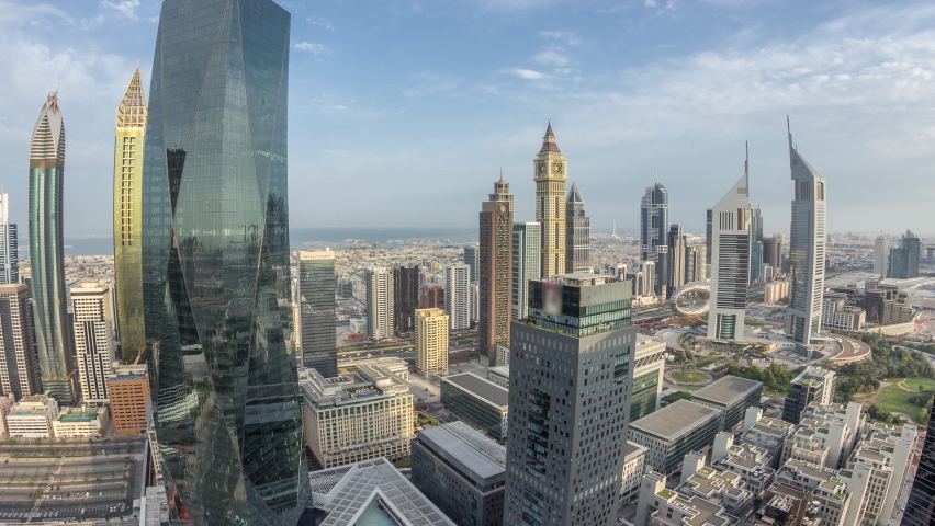 Panorama of futuristic skyscrapers in financial district business center in Dubai on Sheikh Zayed road timelapse. Aerial view from above with clouds on a blue sky